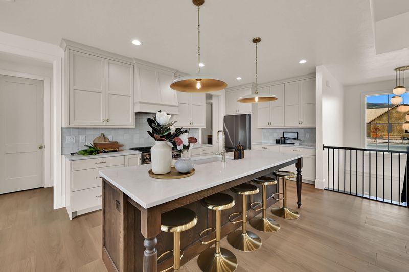 Kitchen island with turned legs and brass stools, pantry door beyond