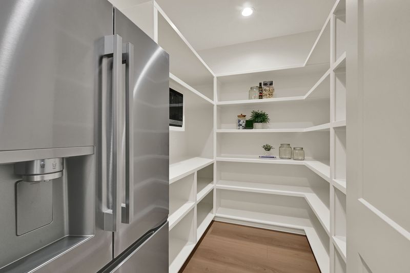 Walk-in pantry with wraparound shelving beside the refrigerator