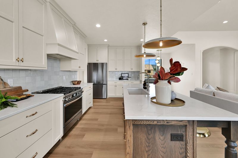 Gas range under a plaster hood with a tiled backsplash and the stained oak island alongside