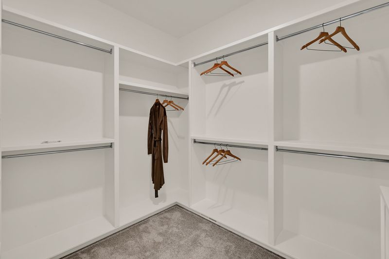 Primary walk-in closet with built-in shelving and hanging on three walls
